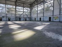 a large empty warehouse is seen with its windows covered in graffiti and shadows on the floor