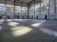 a large empty warehouse is seen with its windows covered in graffiti and shadows on the floor