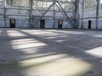 a large empty warehouse is seen with its windows covered in graffiti and shadows on the floor