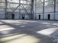 a large empty warehouse is seen with its windows covered in graffiti and shadows on the floor