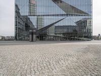 an architectural office building with glass panels on it in the middle of the road, in front of a cobblestone street