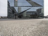 an architectural office building with glass panels on it in the middle of the road, in front of a cobblestone street