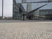 an architectural office building with glass panels on it in the middle of the road, in front of a cobblestone street