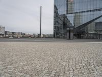 an architectural office building with glass panels on it in the middle of the road, in front of a cobblestone street