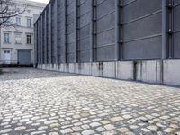 the walkway is made of old cobblestones in front of gray buildings in berlin