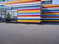 the large multicolor building is painted like a rainbow striped block wall, on top of parking lot