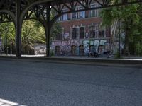 a street under an old metal structure with graffiti on it and people in the shade