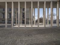 there is an open air building with columns on the wall in front of it and a parking lot to the side of the road