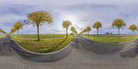 a fisheye lens view of three asphalt roads in a field with trees and a cloudy sky