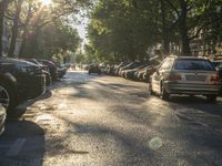 parked cars line the street and people walk on the sidewalk to catch a ride in the sunshine