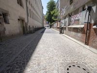 a narrow cobblestone street with graffiti all over it on one side and a red fire hydrant on the other