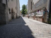 a narrow cobblestone street with graffiti all over it on one side and a red fire hydrant on the other