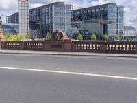 a woman riding a bicycle next to a bunch of buildings across the river from a bridge