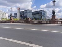 a woman riding a bicycle next to a bunch of buildings across the river from a bridge