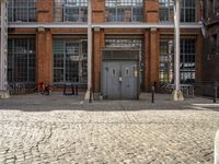 the two doors are in front of the tall brick building in this photo, there is a bench at one end of the path