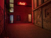 the word hotel glowing brightly red from a dark room in a brick building next to the entrance