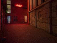 the word hotel glowing brightly red from a dark room in a brick building next to the entrance