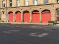 a person on a bicycle is walking down a street past an older brick building that has five red doors