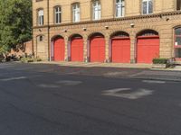 a person on a bicycle is walking down a street past an older brick building that has five red doors