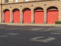 a person on a bicycle is walking down a street past an older brick building that has five red doors