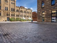 brick courtyard with people on tables and a white umbrellas outside of the building's entrance