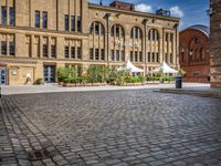 brick courtyard with people on tables and a white umbrellas outside of the building's entrance