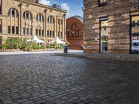 brick courtyard with people on tables and a white umbrellas outside of the building's entrance