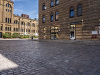 brick courtyard with people on tables and a white umbrellas outside of the building's entrance