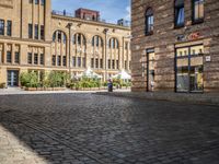 brick courtyard with people on tables and a white umbrellas outside of the building's entrance