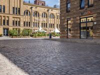 brick courtyard with people on tables and a white umbrellas outside of the building's entrance