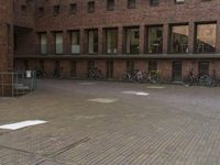 a group of bicycles parked in a brick courtyard near a building and windows with bikes attached to it