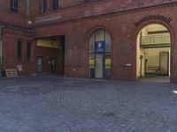 a brick courtyard has a red fire hydrant outside of a large building, the entrance door is to a parking garage