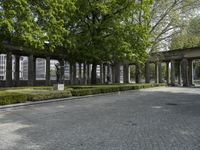 a brick pathway through the ruins of a city park, with stone columns lined by green plants