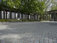 a brick pathway through the ruins of a city park, with stone columns lined by green plants