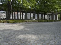 a brick pathway through the ruins of a city park, with stone columns lined by green plants