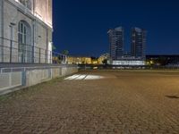 the empty brick road in the dark with buildings in the distance and lights at night