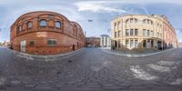 a 360 - shot of some buildings on a brick road with cobblestones and one person walking