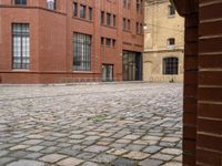 a brick walkway between two red buildings with doors on each side and windows facing one another