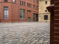 a brick walkway between two red buildings with doors on each side and windows facing one another