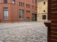 a brick walkway between two red buildings with doors on each side and windows facing one another