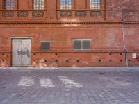 the brick wall of an old building with many windows and small holes on it and a bicycle parked on the street in front of it