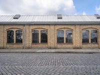 a sidewalk in front of an old brick building and a brick road with lots of windows