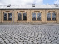 a sidewalk in front of an old brick building and a brick road with lots of windows