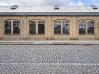 a sidewalk in front of an old brick building and a brick road with lots of windows