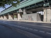 a street in front of a bridge with graffiti on it and cars parked beneath the road