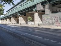 a street in front of a bridge with graffiti on it and cars parked beneath the road