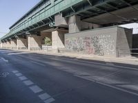 a street in front of a bridge with graffiti on it and cars parked beneath the road