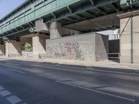 a street in front of a bridge with graffiti on it and cars parked beneath the road