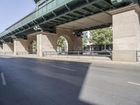 a street in front of a bridge with graffiti on it and cars parked beneath the road