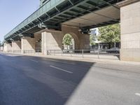 a street in front of a bridge with graffiti on it and cars parked beneath the road